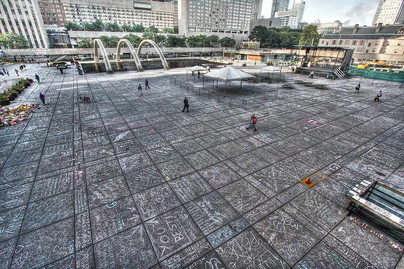 Une photo couleur d’une grande place en béton, le Nathan Phillips Square, comportant des centaines de messages écrits à l’aide de craies de différentes couleurs.