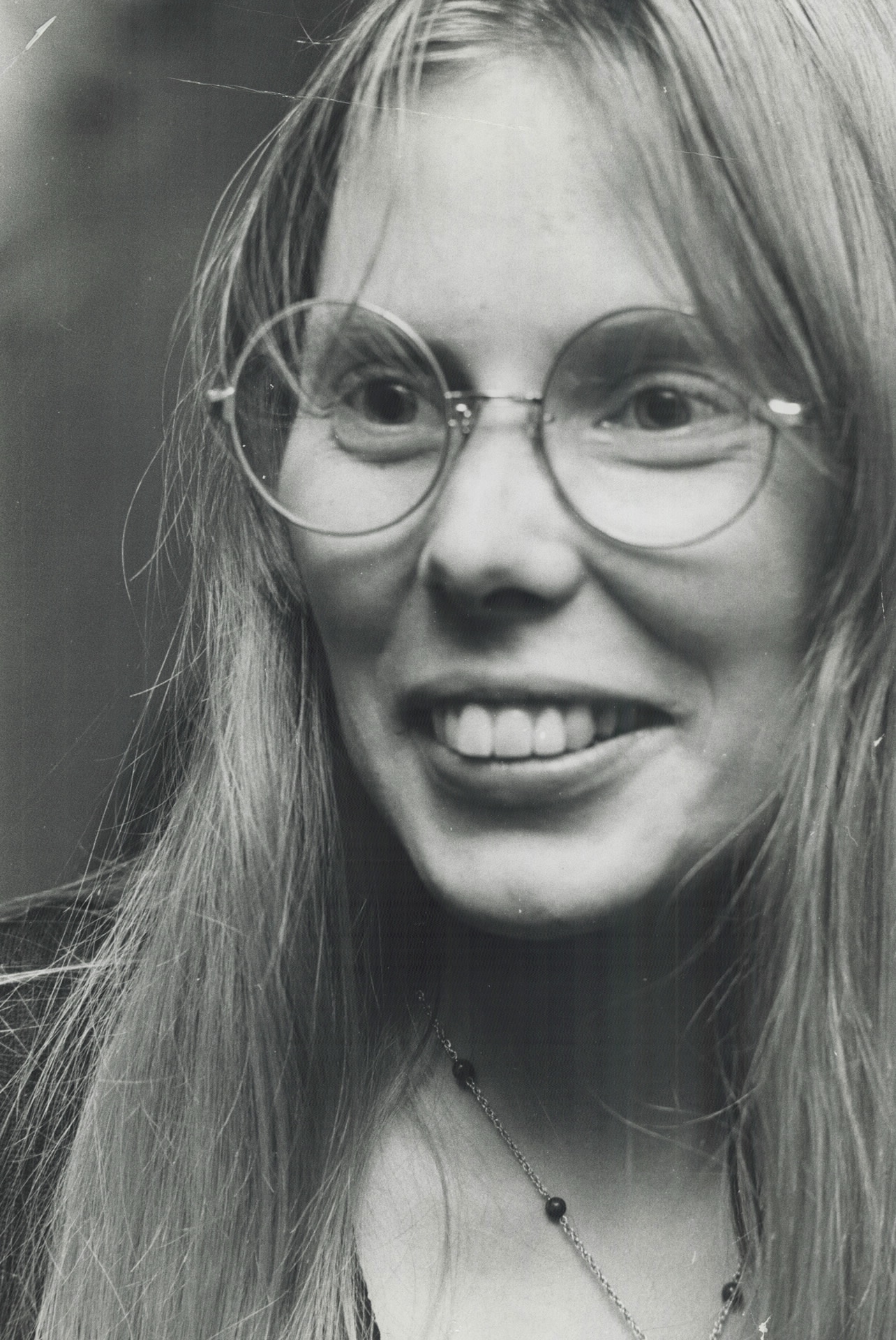 A black and white photo of a woman wearing glasses stares at the camera